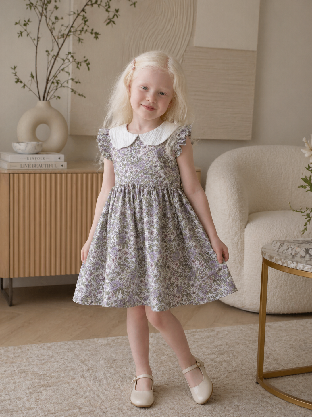 Young girl in a floral dress standing in a cozy living room.